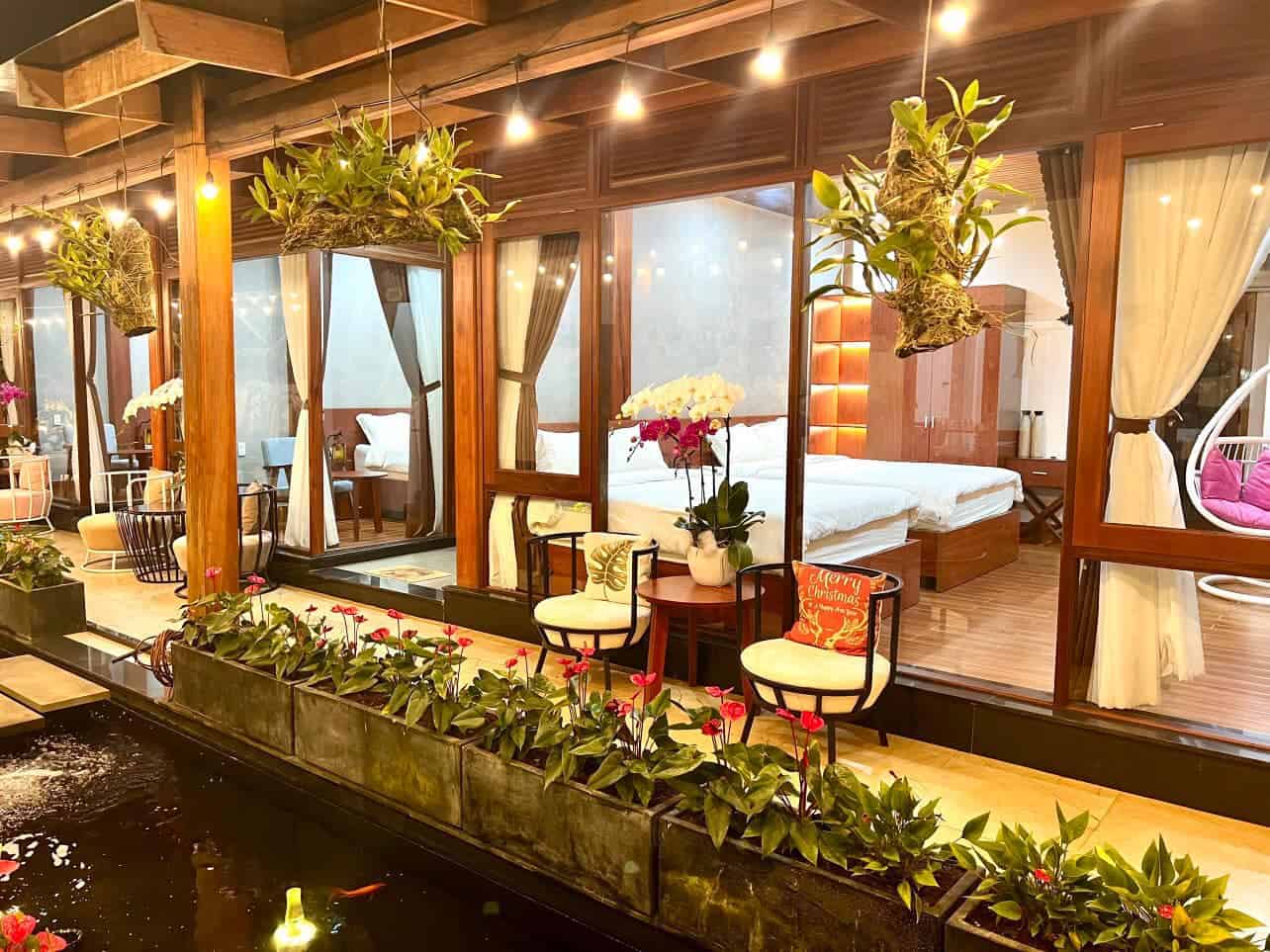 homestay Măng Đen góc nhìn vào các phòng ngủ qua hành lang đặt bộ bàn ghế ngồi ngắm hồ cá coi trang trí nhiều hoa vườn trà homestay