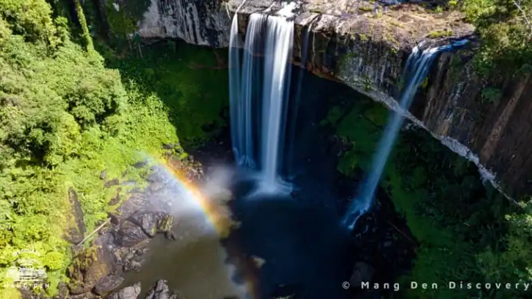 review thác K50 nhìn từ trên cao, dòng thác chảy mạnh, có hiệu ứng cầu vòng, xung quanh là rừng cây hoang sơ