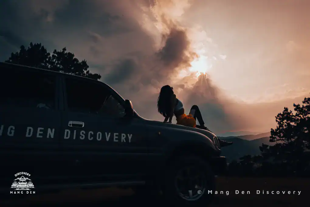 cô gái chụp ảnh cùng hoàng hôn khi ngồi trên nắp capo xe 2 cầu tại Kon Tu Rằng Măng Đen trong tour du lịch Măng Đen photo tour họ quan tâm đến thời tiết Măng Đen mùa mưa