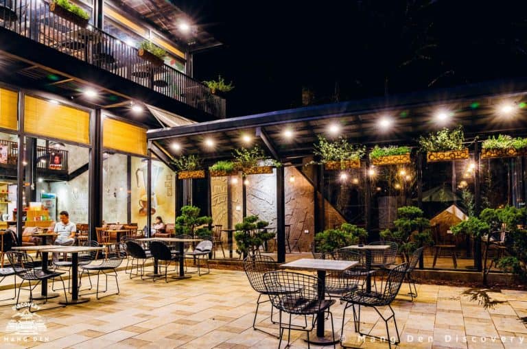 quán cafe Măng Đen với nhiều bàn, ghế, khách thưởng thức có đèn, và cây trang trí tại Măng Đen được nhiều du khách quan tâm, tìm kiếm
