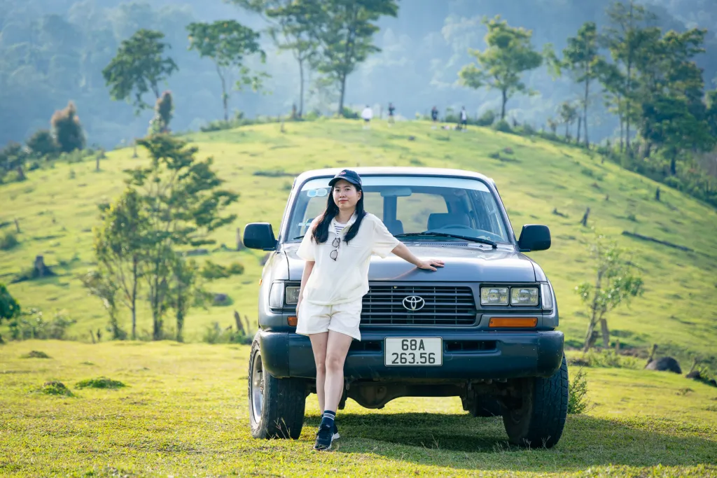 cô gái chụp ảnh cùng xe 2 cầu của măng đen discovery tại đồi cỏ kon vơng kia khi đến đây tham quan vào buổi trưa, sau lưng là cây và đồi núi