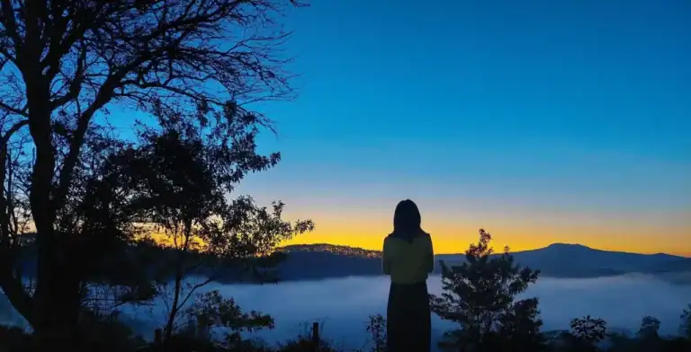 DU LỊCH MĂNG ĐEN DỊP LỄ 30/4 & 1/5 - KINH NGHIỆM TRỌN VẸN A–Z 1 cô gái đứng ngắm mây bên núi rừng tại quán cafe Konoha tại Măng Đen dành cho những ai cần quán cafe săn mây khi du lịch Măng Đen dịp Lễ