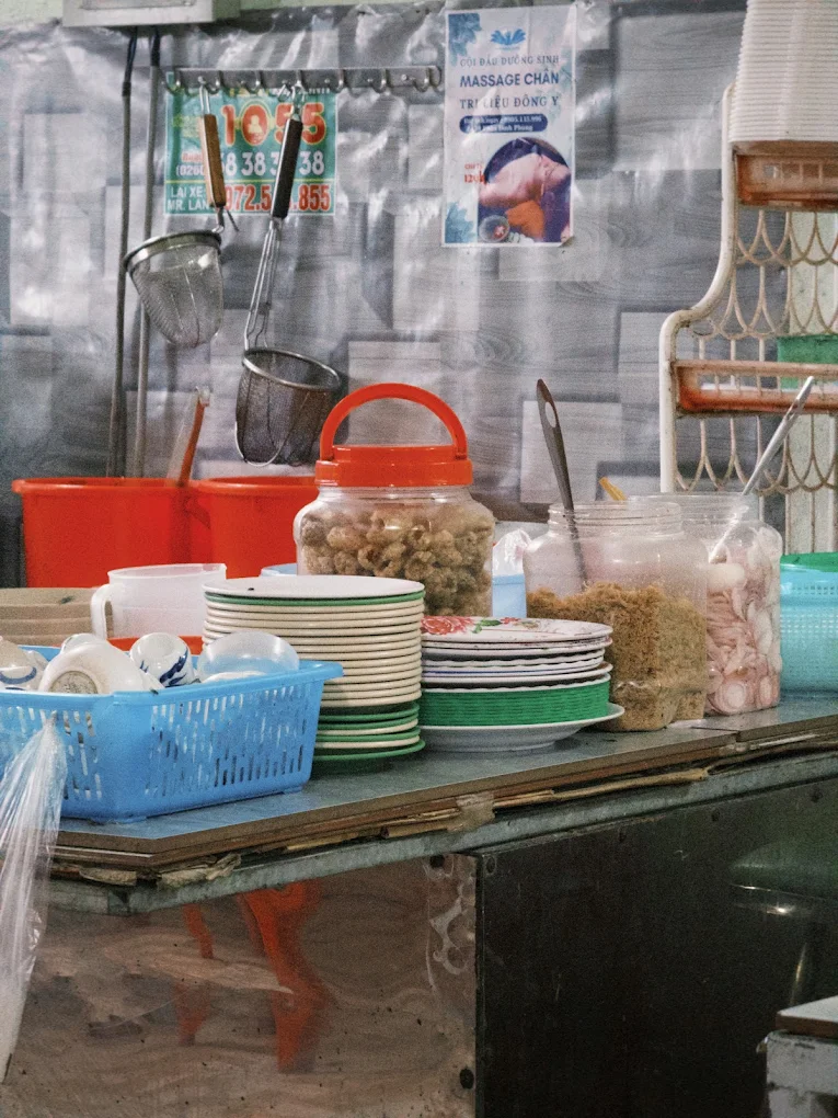 Quầy chuẩn bị topping tại Quán Bà Bảy Măng Đen với bát đĩa, tóp mỡ và hành ngâm
