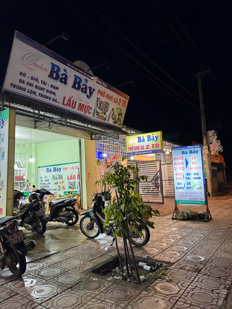 Quán Bà Bảy Măng Đen vào buổi tối với bảng hiệu sáng đèn và xe máy trước cửa