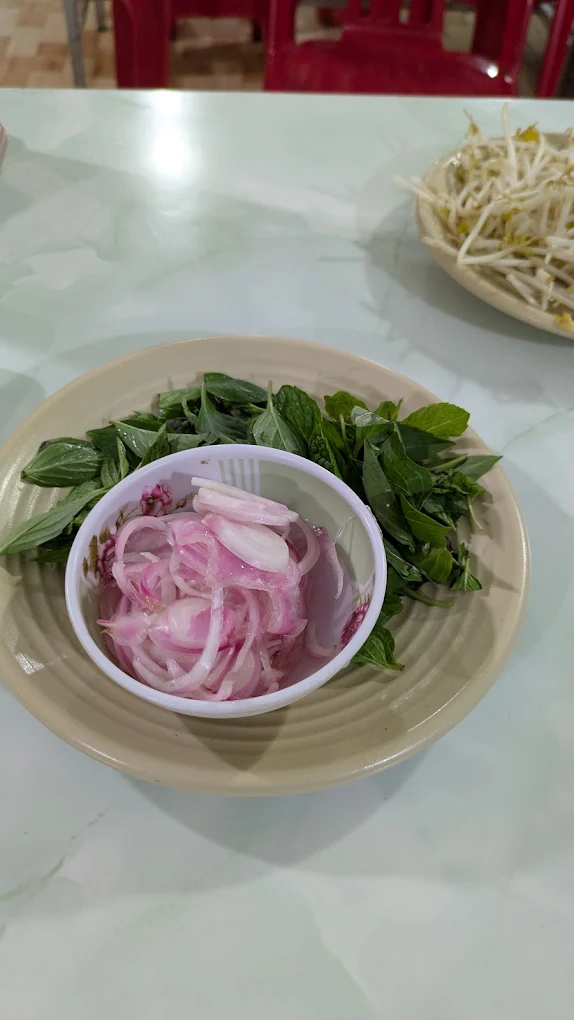 Đĩa hành ngâm và rau thơm ăn kèm phở tại Quán Bà Bảy Măng Đen